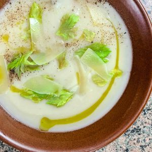 A bowl of celery root soup with a drizzle of olive oil, celery leaves, and black pepper