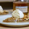 A slice of apple galette with a scoop of ice cream and a bottle of single malt scotch in the background