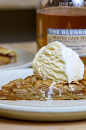 A slice of apple galette with a scoop of ice cream and a bottle of single malt scotch in the background