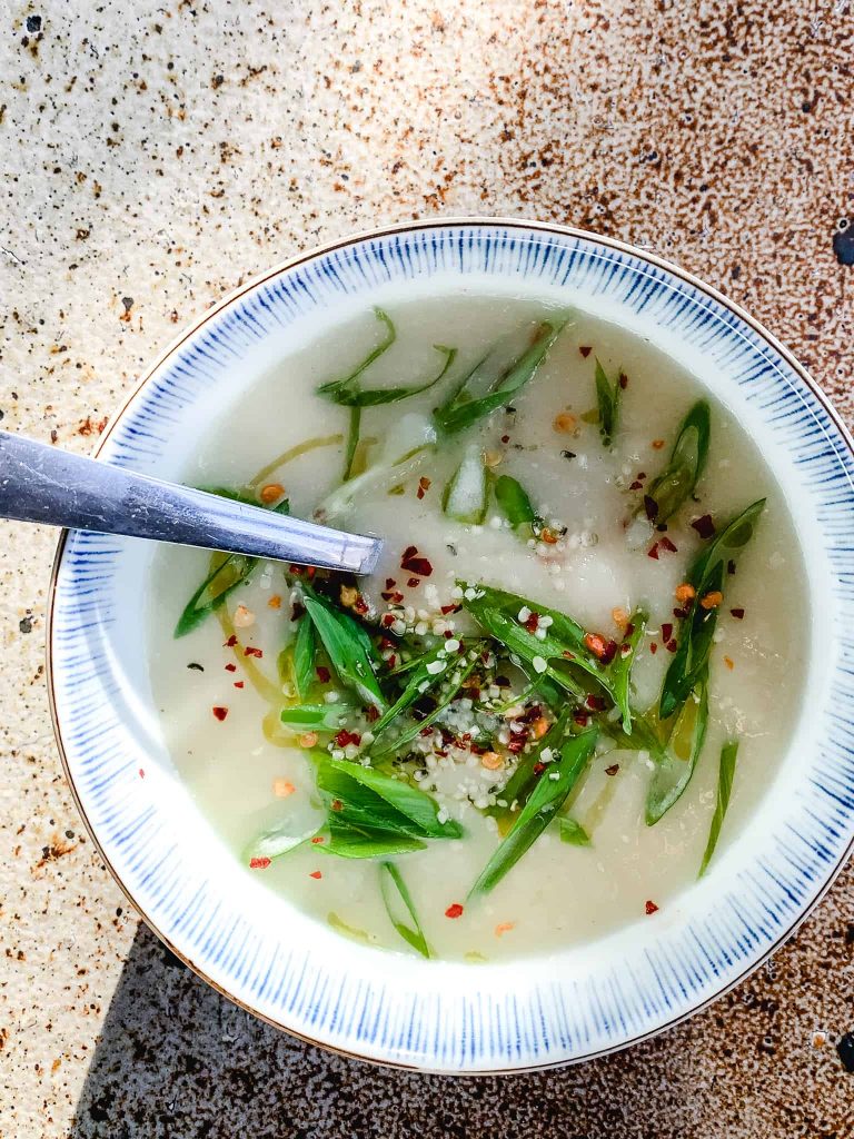Delicious celery root soup in a bowl, garnished with green onions and chili flakes.