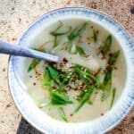 Delicious celery root soup in a bowl, garnished with green onions and chili flakes.