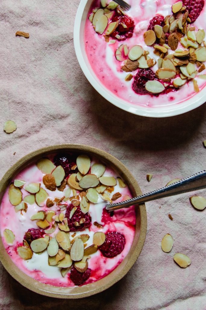 two bowls of plain yogurt with frozen berries and sliced almonds.