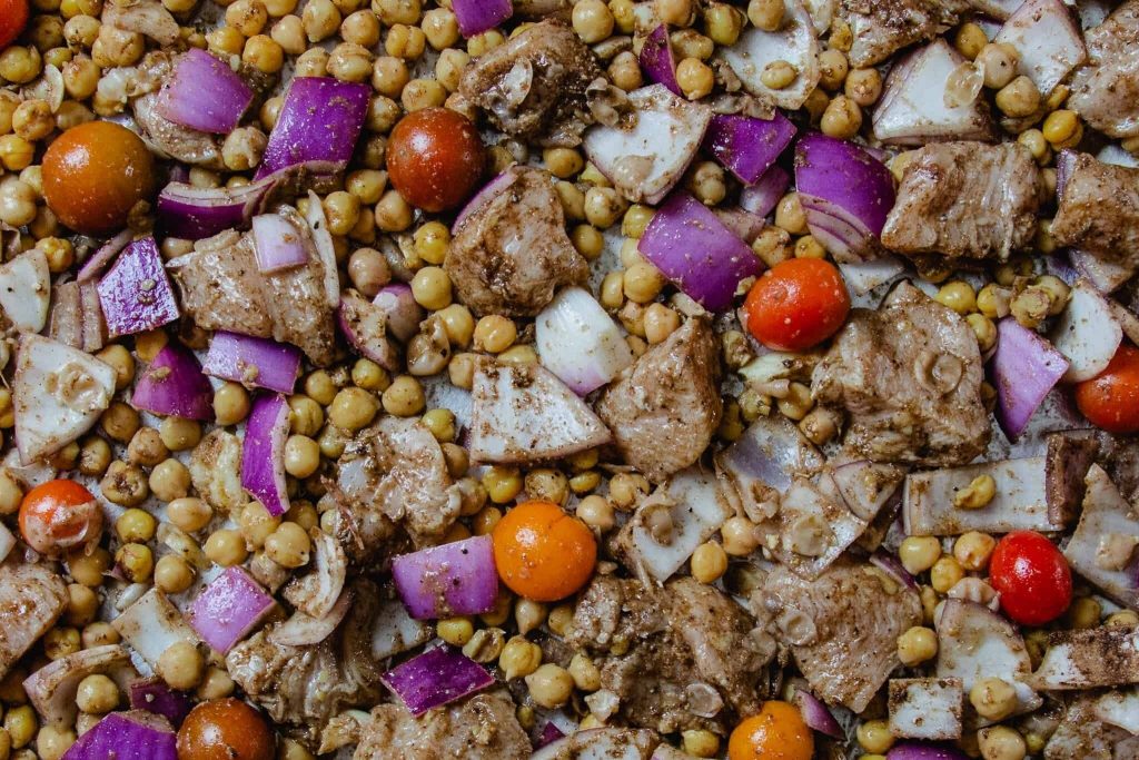 A sheet pan with roasted cubed chicken, chickpeas, red onions & cherry tomatoes 