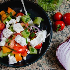 Bulgarian Shopska Salad in a blue bowl with some red onion an cherry tomatoes on the side