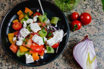 Bulgarian Shopska Salad in a blue bowl with some red onion an cherry tomatoes on the side