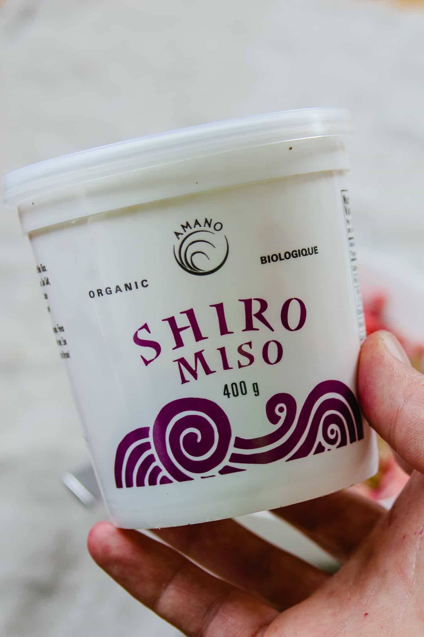 A woman holds a 400g container of Shiro Miso.