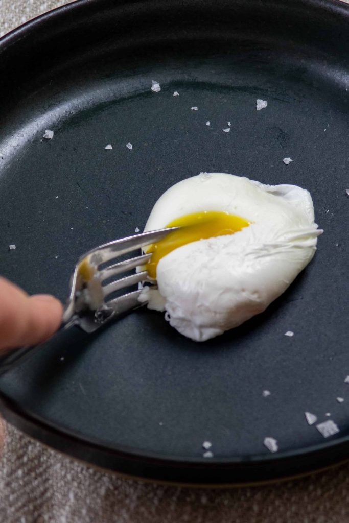 cutting into a soft poached egg on a plate