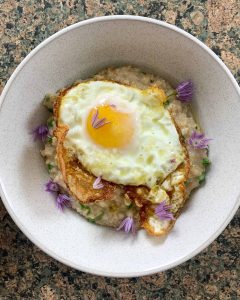 Bowl of savoury porridge with a fried egg and chive flowers