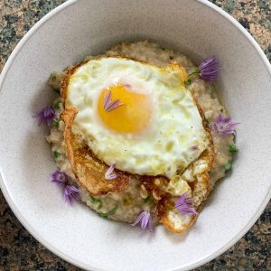 Bowl of savoury porridge with a fried egg and chive flowers