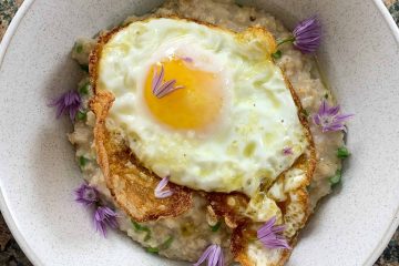 Bowl of savoury porridge with a fried egg and chive flowers