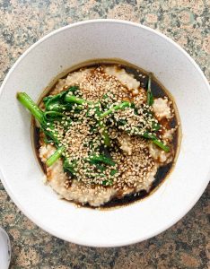 A bowl of savoury porridge with greens and sesame seeds