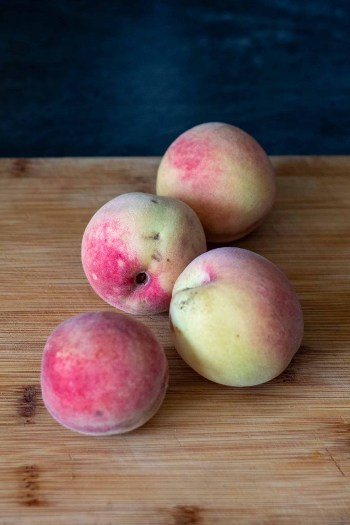 four peaches on a cutting board.