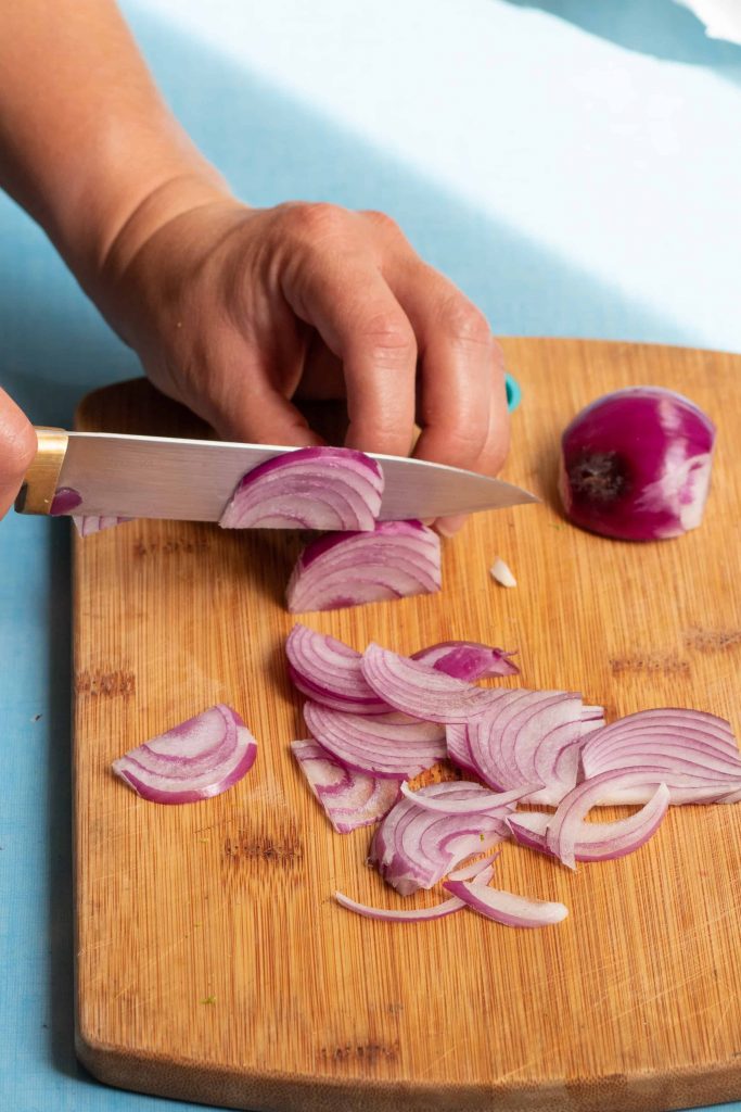 a red onion being sliced on a cutting board.