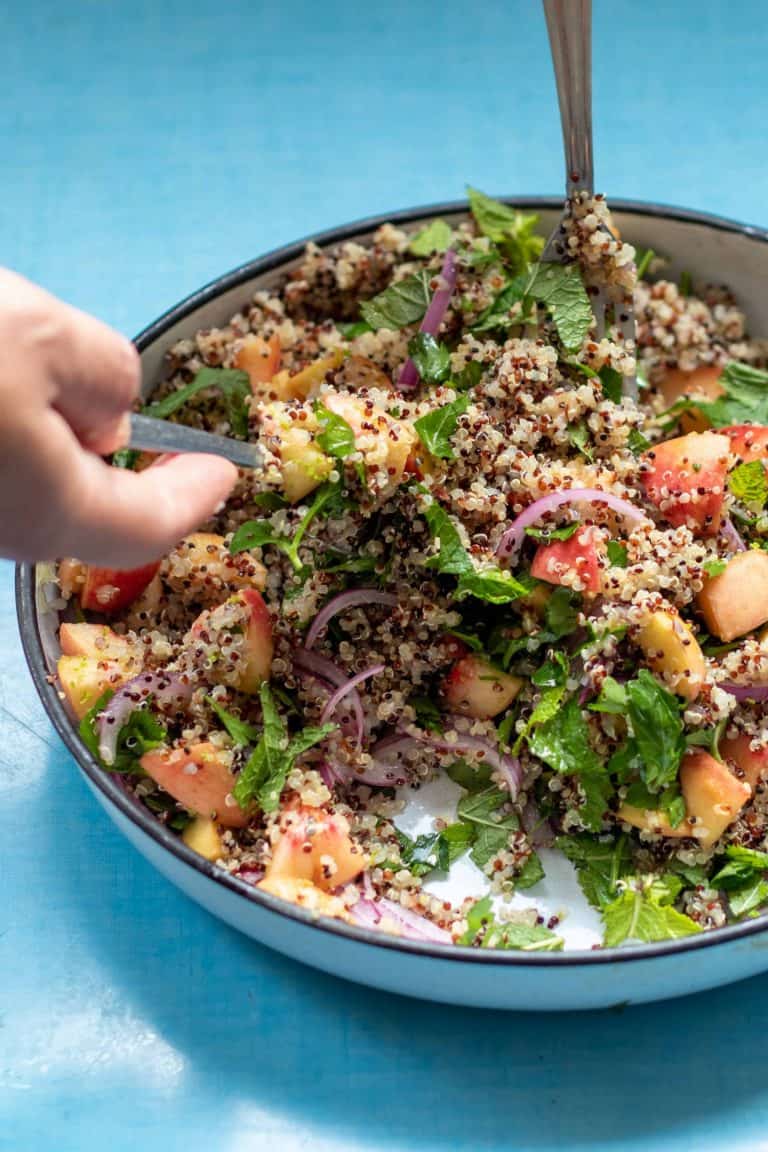 A large bowl of peach quinoa salad being served on a blue table.