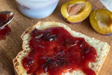 plum and ginger jam on toast with a cut fresh plum next to it.