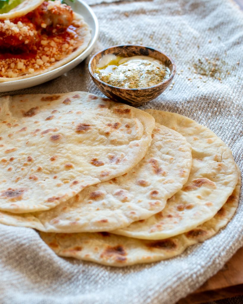 a stack of flatbread on a linen tablecloth with yogurt dip in the background.