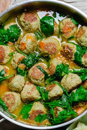 a pan of turkey meatballs in broth with wilted spinach.