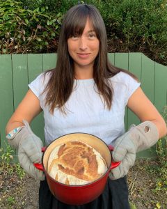 a proud bread baker holding a loaf of bread baked in a Dutch oven.