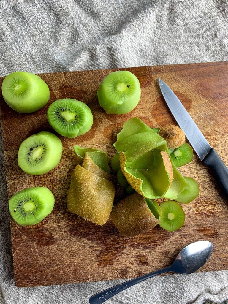 peeled kiwis and their skins on a cutting board.