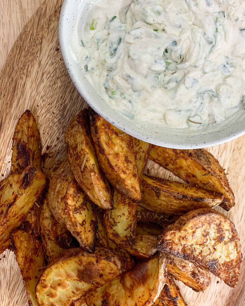 A bowl of sour cream and onion dip with a pile of crispy wedge potatoes on the side.
