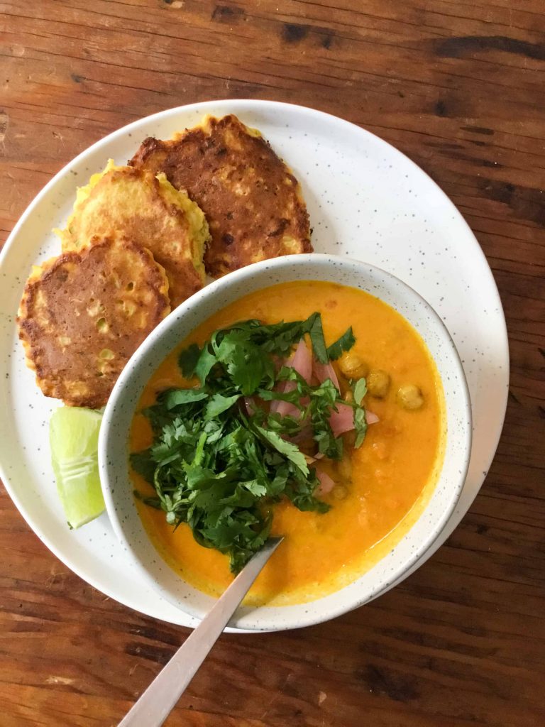 Carrot tahini soup in a bowl with toppings, with vegetable fritters and a lime wedge on the side.