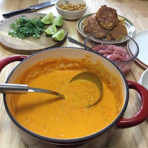 A pot of carrot tahini soup on a table with toppings laid out.