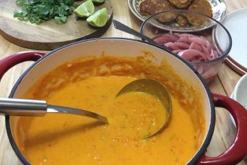 A pot of carrot tahini soup on a table with toppings laid out.