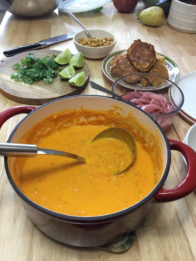 A pot of carrot tahini soup on a table with toppings laid out.