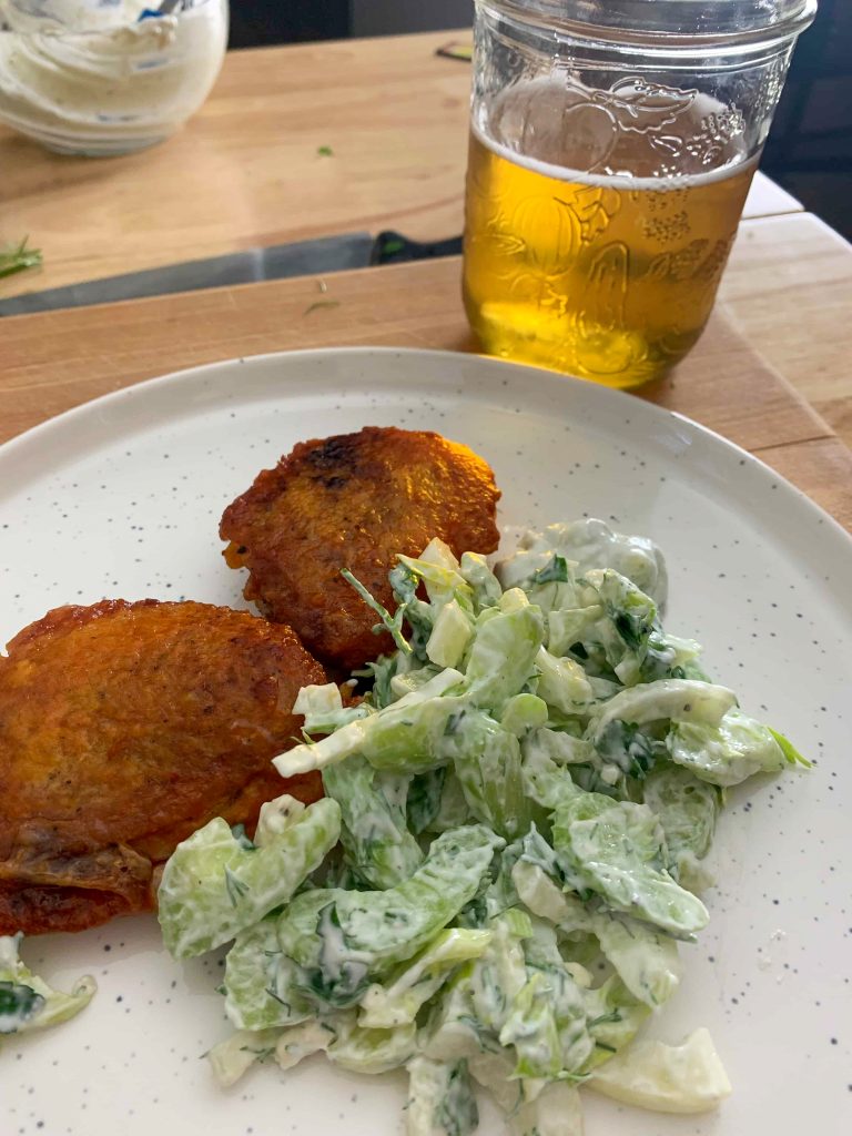 a plate of chicken thighs with celery salad on the side, and a glass of beer.