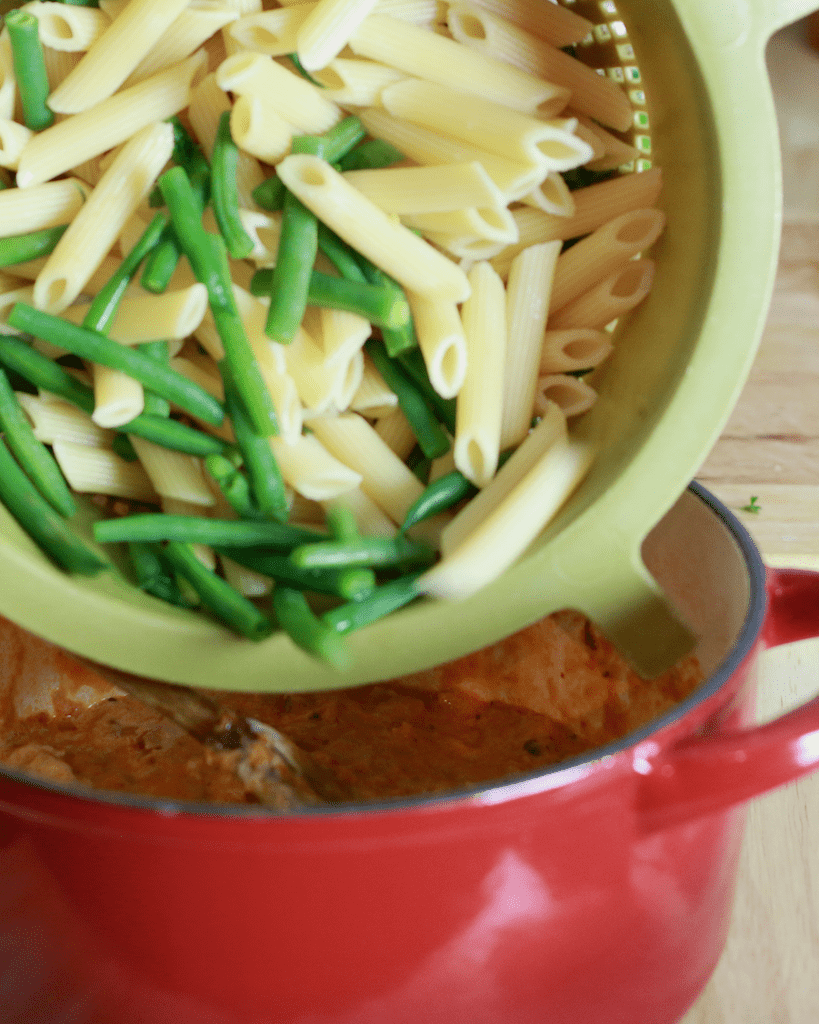 adding pasta and green beans back to the pot.