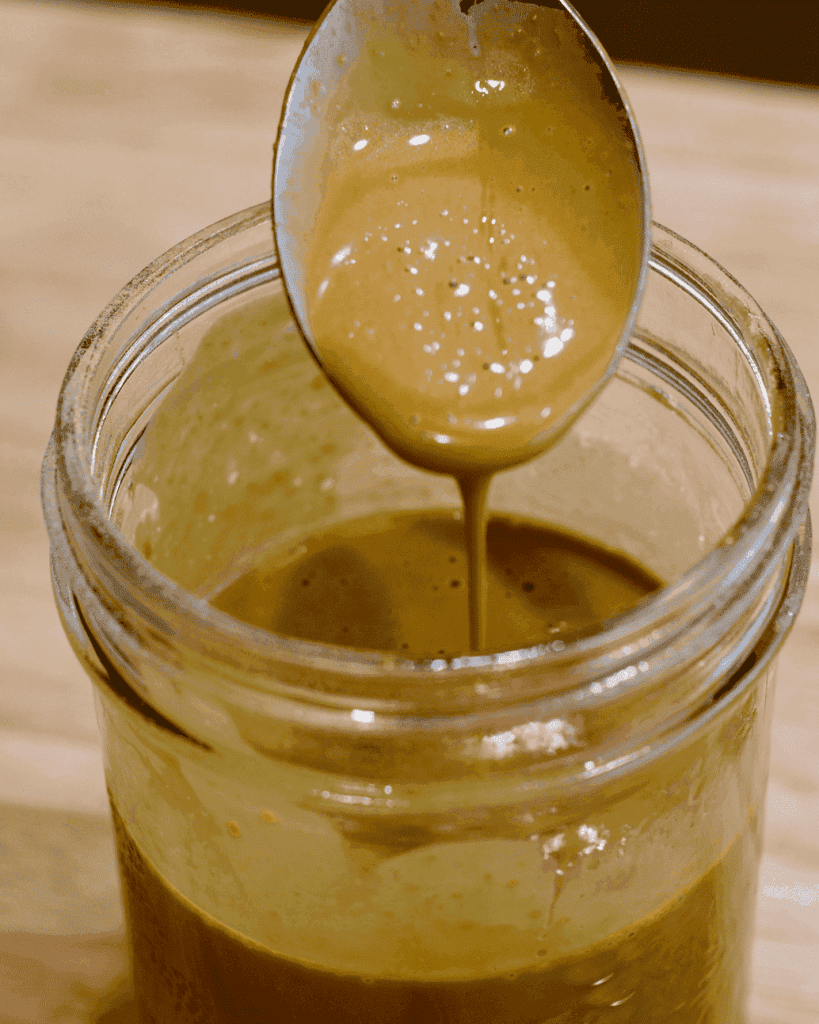 Creamy nutritional yeast dressing dripping off a spoon into a glass jar.