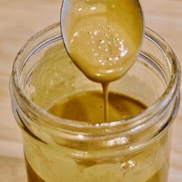 Creamy nutritional yeast dressing dripping off a spoon into a glass jar.