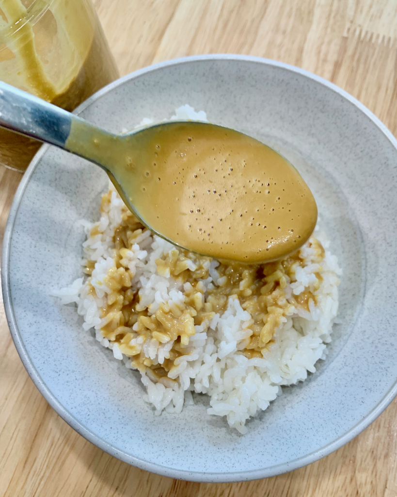 Drizzling nutritional yeast dressing over steamed white rice in a bowl.