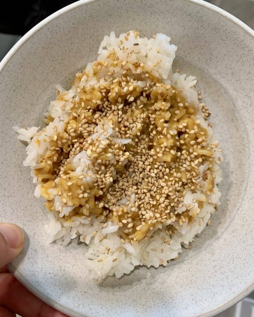 Pouring nutritional yeast dressing over baby spinach in a bowl.