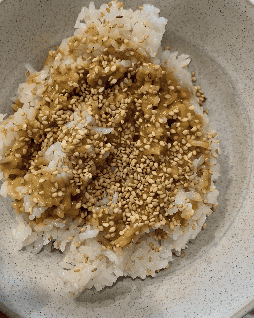 Steamed white rice in a bowl with nutritional yeast dressing and toasted sesame seeds on top.