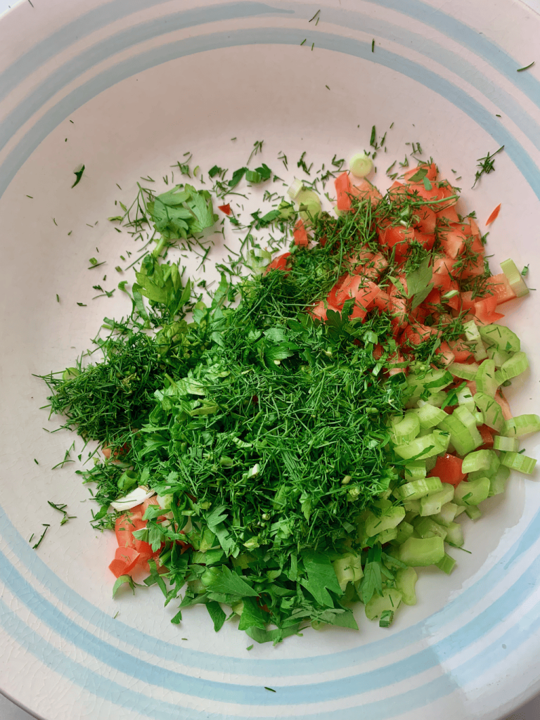 Chopped fresh celery, red bell pepper, dill, and parsley in a bowl.