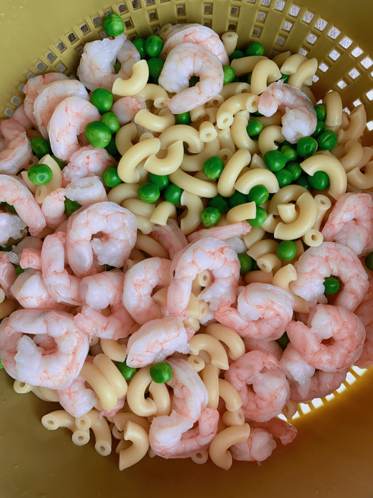 Shrimp, macaroni, and peas in a green colander.