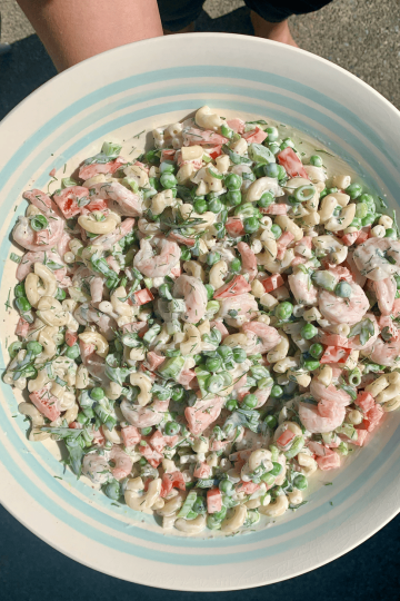 A woman holding a bowl of shrimp macaroni salad, ready to serve it up.