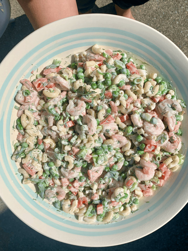 A woman holding a bowl of shrimp macaroni salad, ready to serve it up.
