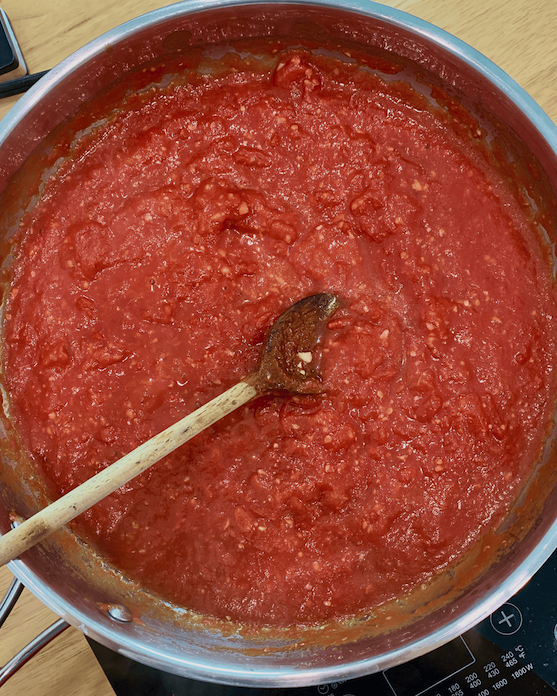 A pan of hearty marinara sauce with a wooden spoon.