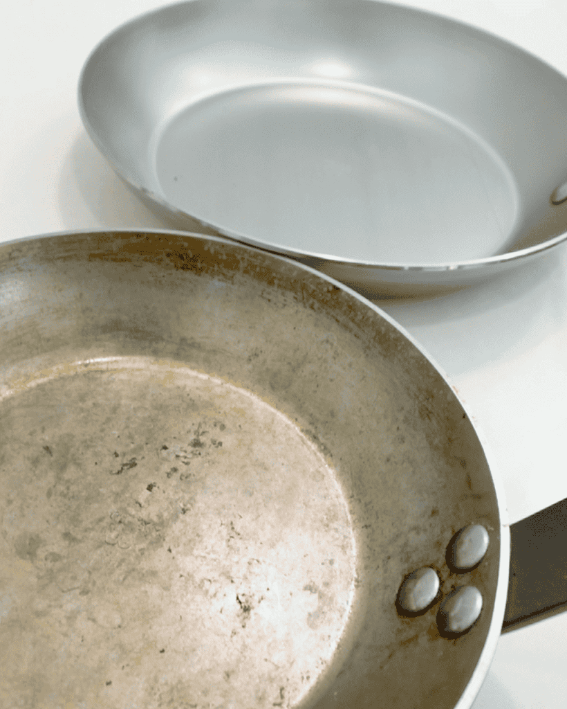 A seasoned carbon steel pan next to a brand new carbon steel pan.