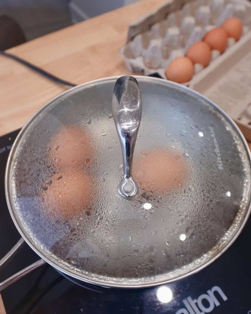 A covered pot with 3 eggs steaming inside.