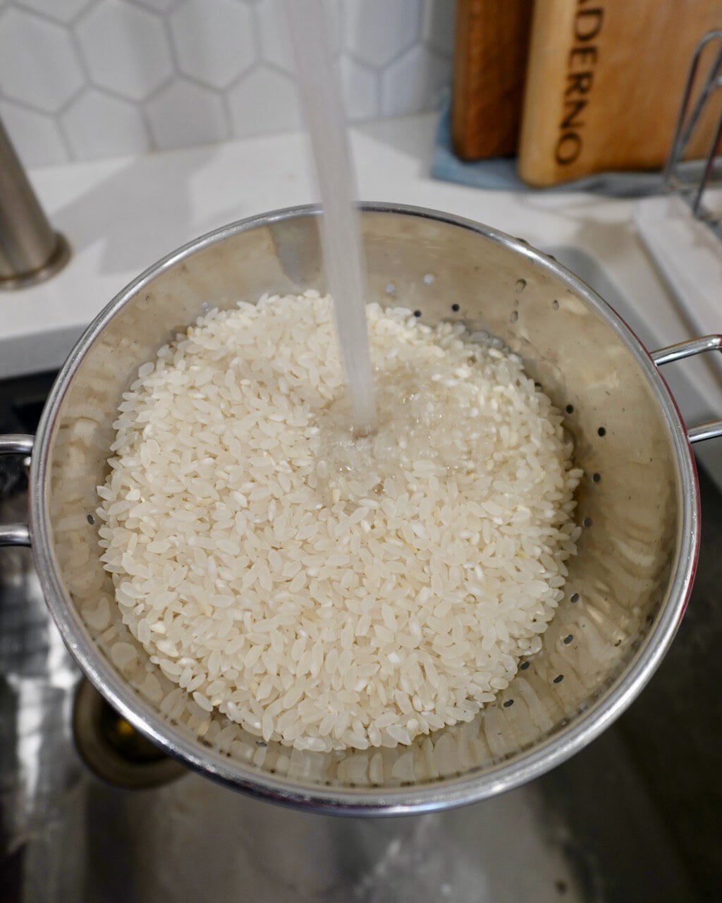 A sieve with rice being rinsed with cold water from the tap.