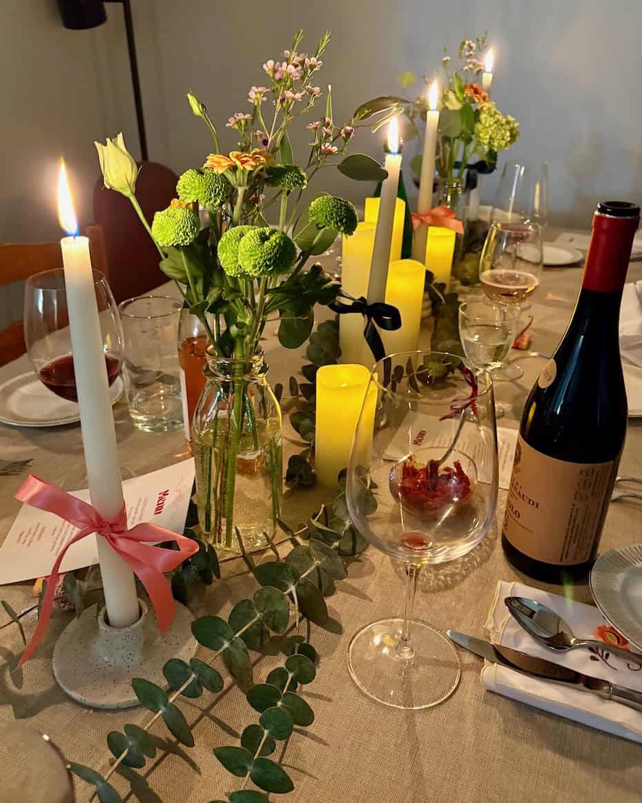 a table set for a dinner party with candles, flowers, and glasses of red wine.