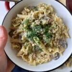 A woman holding a bowl of stroganoff topped with fresh dill.