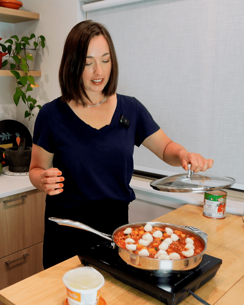 A woman lifts a lid off of a pot of tomato gnocchi.