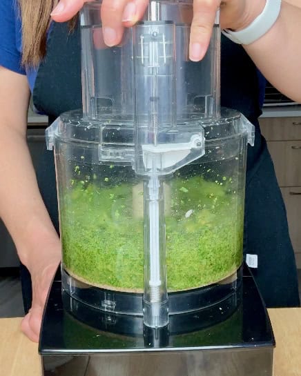 A woman grinds pesto in a food processor.