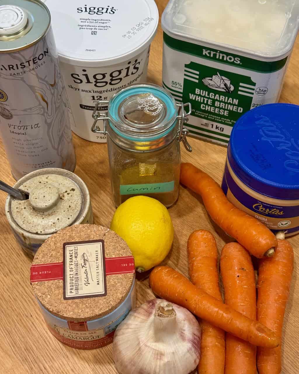Ingredients for creamy roasted carrot dip with feta and tahini on a wooden surface.