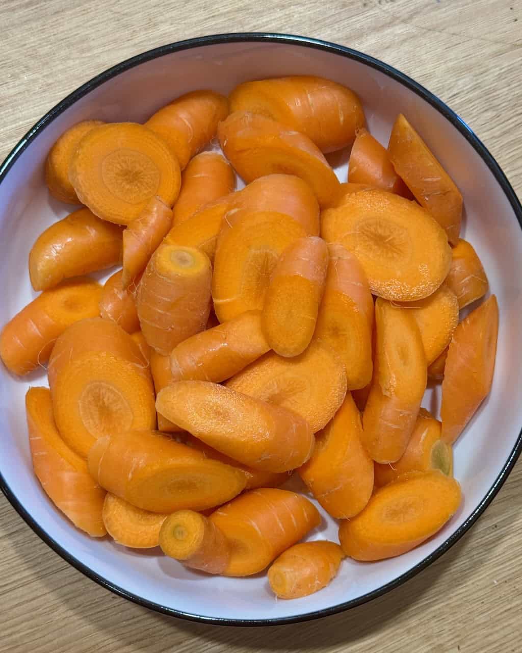 Freshly sliced orange carrots in a white bowl for a creamy roasted carrot dip.