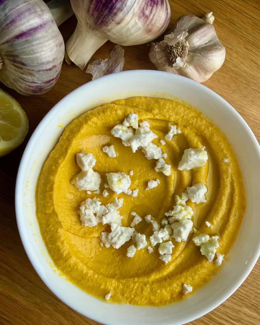 Creamy roasted carrot dip topped with crumbled feta in a white bowl.